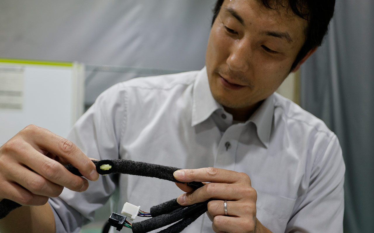 Funasaka examining a wiring harness, whose stiffness once became the root cause of a water leak discovered during pre-production testing.